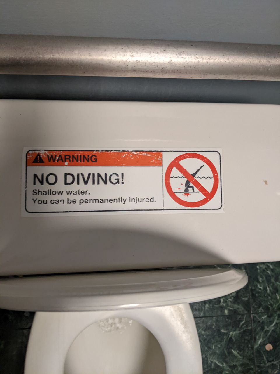A label reading "WARNING, NO DIVING! Shallow water. you can be permanently injured"
that is affixed to a toliet lid